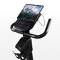 Black upright exercise bike with tablet holder displaying mountain landscape, digital console with blue display, curved handl