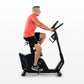 Man in coral t-shirt and black shorts riding black upright exercise bike with blue accents on white background