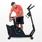 Man wearing coral t-shirt and black shorts using black upright exercise bike with blue accents on white background