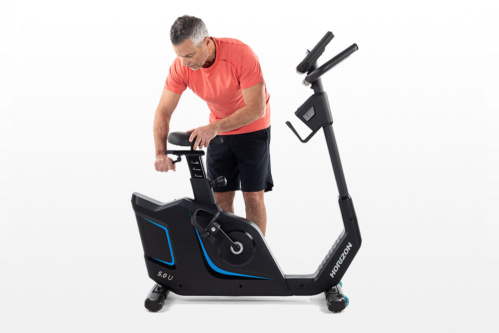 Man wearing coral t-shirt and black shorts using black upright exercise bike with blue accents on white background