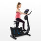 Woman in pink tank top and black leggings using black upright exercise bike with blue accents and digital display console