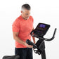 Man wearing coral t-shirt using upright exercise bike with digital console display on white background