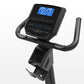 Black upright exercise bike with curved handlebars, foot pedals, and blue digital display console showing workout metrics