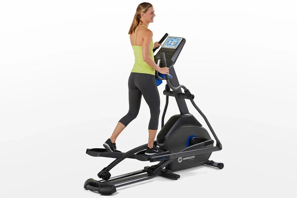 Woman wearing lime green tank top and black capris using black and blue Horizon 7.0 AE elliptical with digital display consol