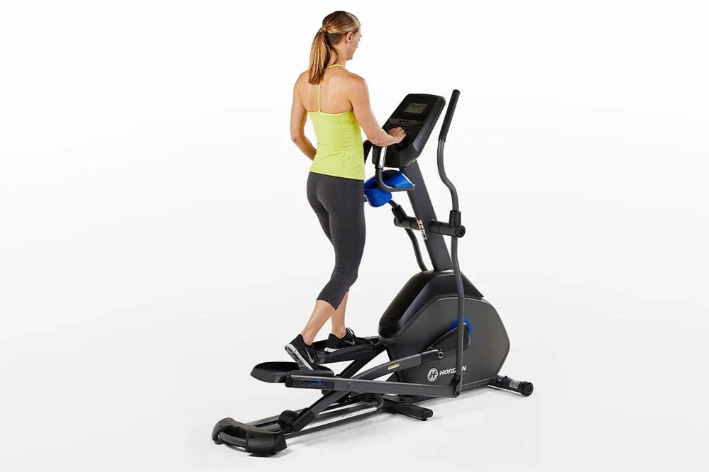 Woman wearing neon yellow tank top and black leggings using black Horizon elliptical machine with blue accents on white backg