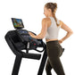 Woman using black Horizon 7.0 AT treadmill with touchscreen display, wearing light gray sports bra and olive leggings