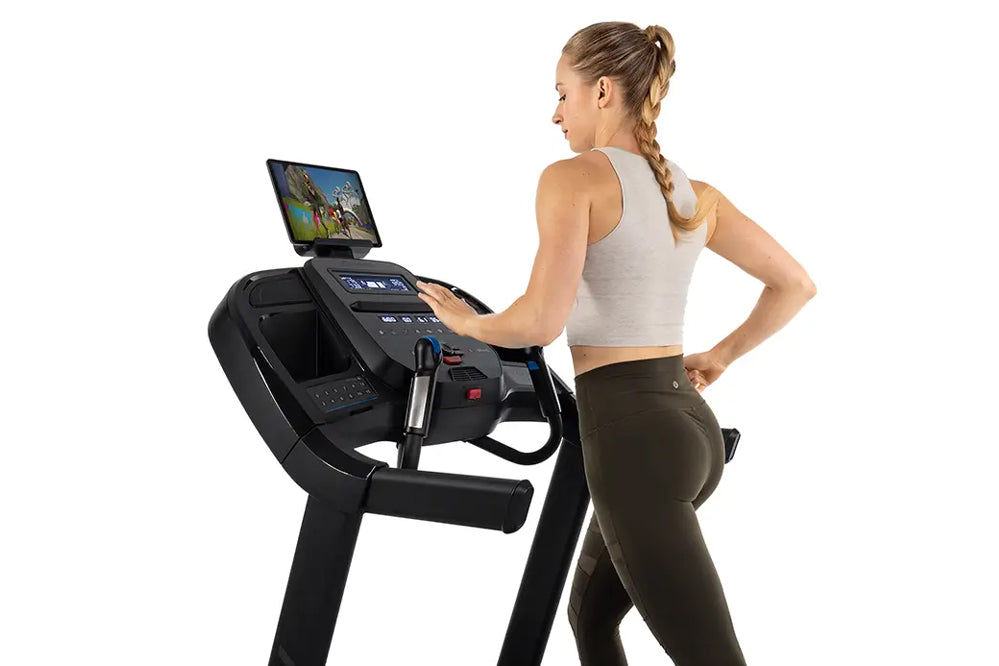 Woman using black Horizon 7.0 AT treadmill with touchscreen display, wearing light gray sports bra and olive leggings