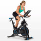 Woman wearing turquoise sports bra and black shorts riding black and blue indoor stationary bike with digital display on whit