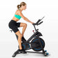 Woman wearing turquoise sports bra and black shorts riding black Horizon 7.0 IC indoor cycle with blue accents on white backg