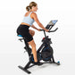Woman wearing light blue sports bra and black shorts riding black and blue stationary exercise bike with tablet holder on whi