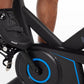 Black cycling shoe with perforated leather and Boa dial closure, worn on stationary bike pedal with blue-rimmed wheel visible