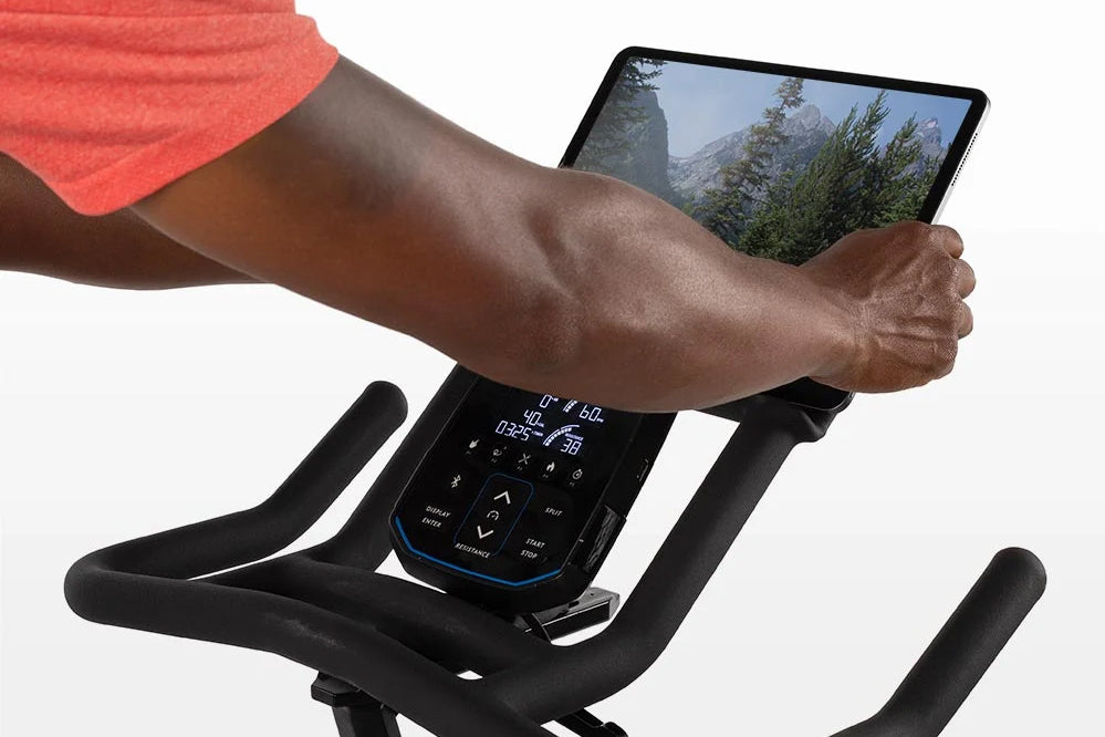 Person wearing coral tank top on Horizon 7.0 IC stationary bike with digital console display and tablet holder showing mounta