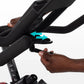 Black stationary bike handlebars with turquoise adjustment arrows displayed, hands gripping bars to show adjustability