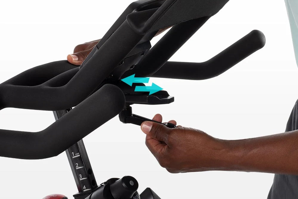 Black stationary bike handlebars with turquoise adjustment arrows displayed, hands gripping bars to show adjustability