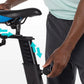 Black and blue stationary exercise bike seat with adjustable height and resistance dial, shown with model demonstrating adjus