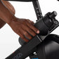 Black stationary indoor cycle handlebar with numbered resistance dial, hand gripping handle during workout