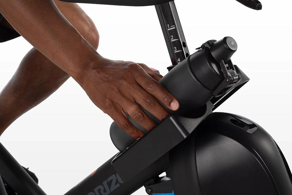 Black stationary indoor cycle handlebar with numbered resistance dial, hand gripping handle during workout