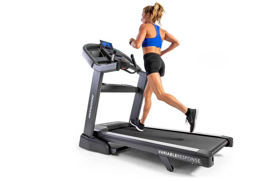 Woman running on Horizon 7.8 AT treadmill wearing blue sports bra and black shorts, white sneakers, on white background