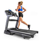 Woman running on Horizon treadmill with blue sports bra and black shorts, machine has digital display and black running belt