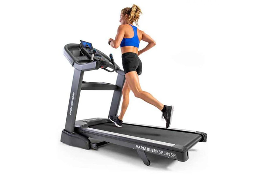 Woman running on Horizon treadmill with blue sports bra and black shorts, machine has digital display and black running belt