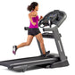 Woman running on black Horizon 7.8 AT treadmill, wearing magenta tank top and black shorts, on white background