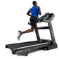 Man running on black Horizon treadmill with digital display, wearing blue tank top and black shorts, on white background