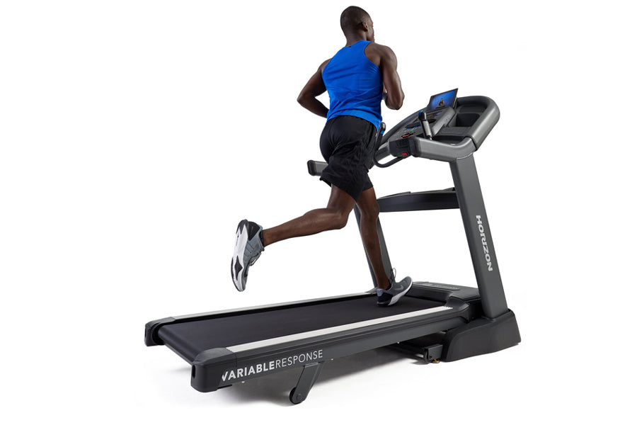 Man running on black Horizon treadmill with digital display, wearing blue tank top and black shorts, on white background
