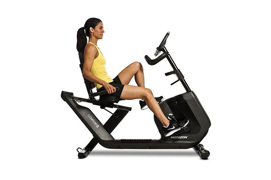 Woman in yellow tank top and black shorts seated on black Horizon recumbent exercise bike with foot pedals and handlebar grip