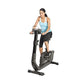 Woman wearing light blue tank top and black capris using upright exercise bike with digital console on white background