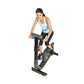 Woman wearing light blue tank top and black leggings riding black upright exercise bike on white background