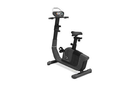 Black upright exercise bike with digital display console, handlebars, padded seat, and foot pedals on white background