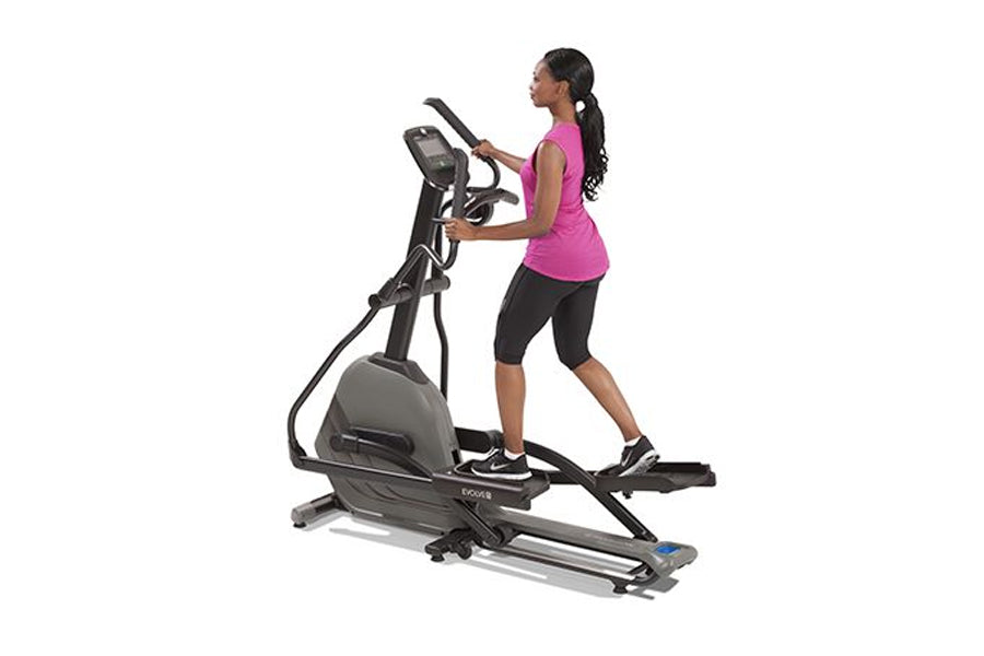 Woman in magenta tank top and black capris using black and gray elliptical machine with digital display on white background