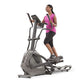Woman wearing pink tank top and black capris using gray and black Horizon Evolve elliptical machine on white background