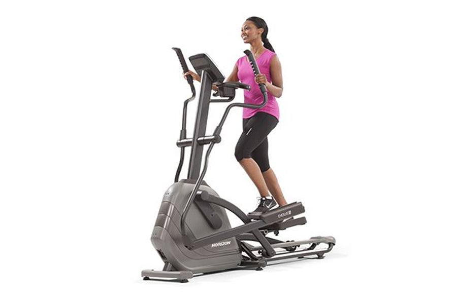 Woman wearing pink tank top and black capris using gray and black Horizon Evolve elliptical machine on white background