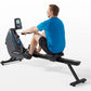 Man in blue shirt using black and gray Horizon rowing machine with digital display on white background