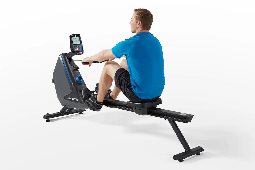 Man in blue shirt using black and gray Horizon rowing machine with digital display on white background