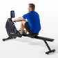 Man in blue shirt using black Horizon Oxford 6 rowing machine with digital display on white background