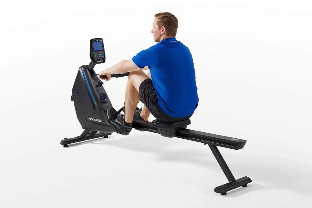 Man in blue shirt using black Horizon Oxford 6 rowing machine with digital display on white background