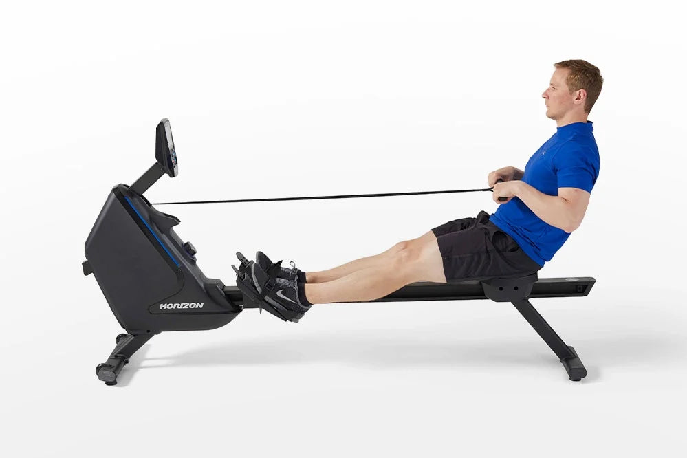 Man in blue shirt and black shorts using black Horizon Oxford 6 rowing machine with extended arms pulling resistance cord