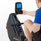 Man in blue shirt using black Horizon rowing machine with digital console display showing workout metrics