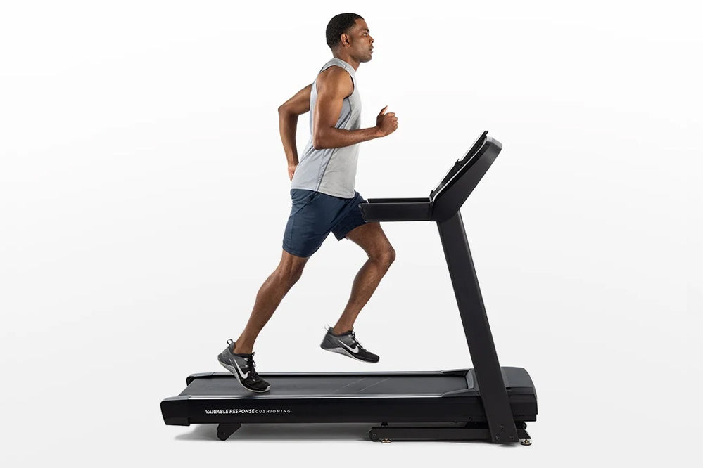 Man running on black Horizon T101 folding treadmill, wearing gray tank top and navy shorts