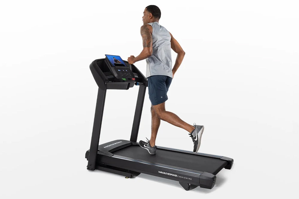 Man running on black Horizon T101 folding treadmill with blue touchscreen display against white background