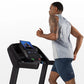 Man running on black Horizon T101 folding treadmill with blue display screen, wearing gray sleeveless shirt and navy shorts