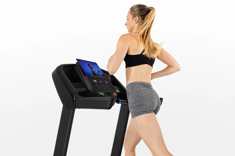 Woman wearing black sports bra and gray shorts running on black Horizon T101 folding treadmill with digital display against w