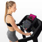 Woman in black sports bra and gray shorts using black Horizon folding treadmill with pink display screen on white background