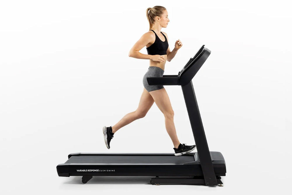 Woman running on black Horizon T101 folding treadmill wearing black sports bra and gray shorts, white background