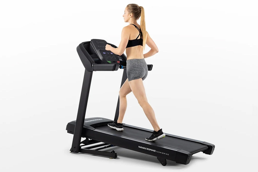 Woman in black sports bra and gray shorts running on black Horizon T101 folding treadmill against white background