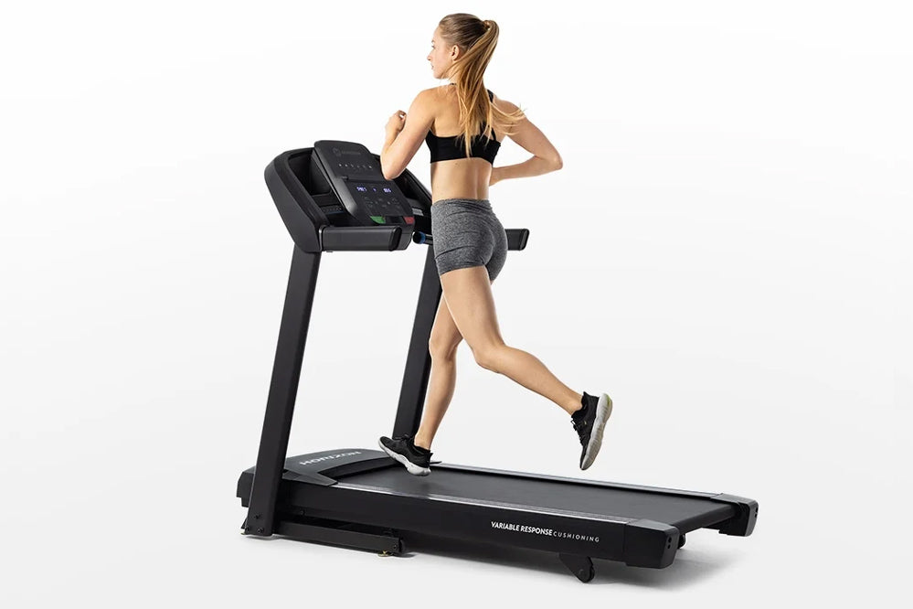 Woman running on black Horizon T101 folding treadmill with digital console, wearing gray shorts and black sports bra