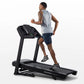 Man running on black folding treadmill with digital display, wearing gray sleeveless shirt and navy shorts