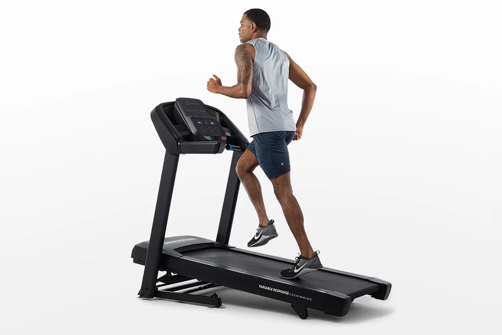 Man running on black folding treadmill with digital display, wearing gray sleeveless shirt and navy shorts